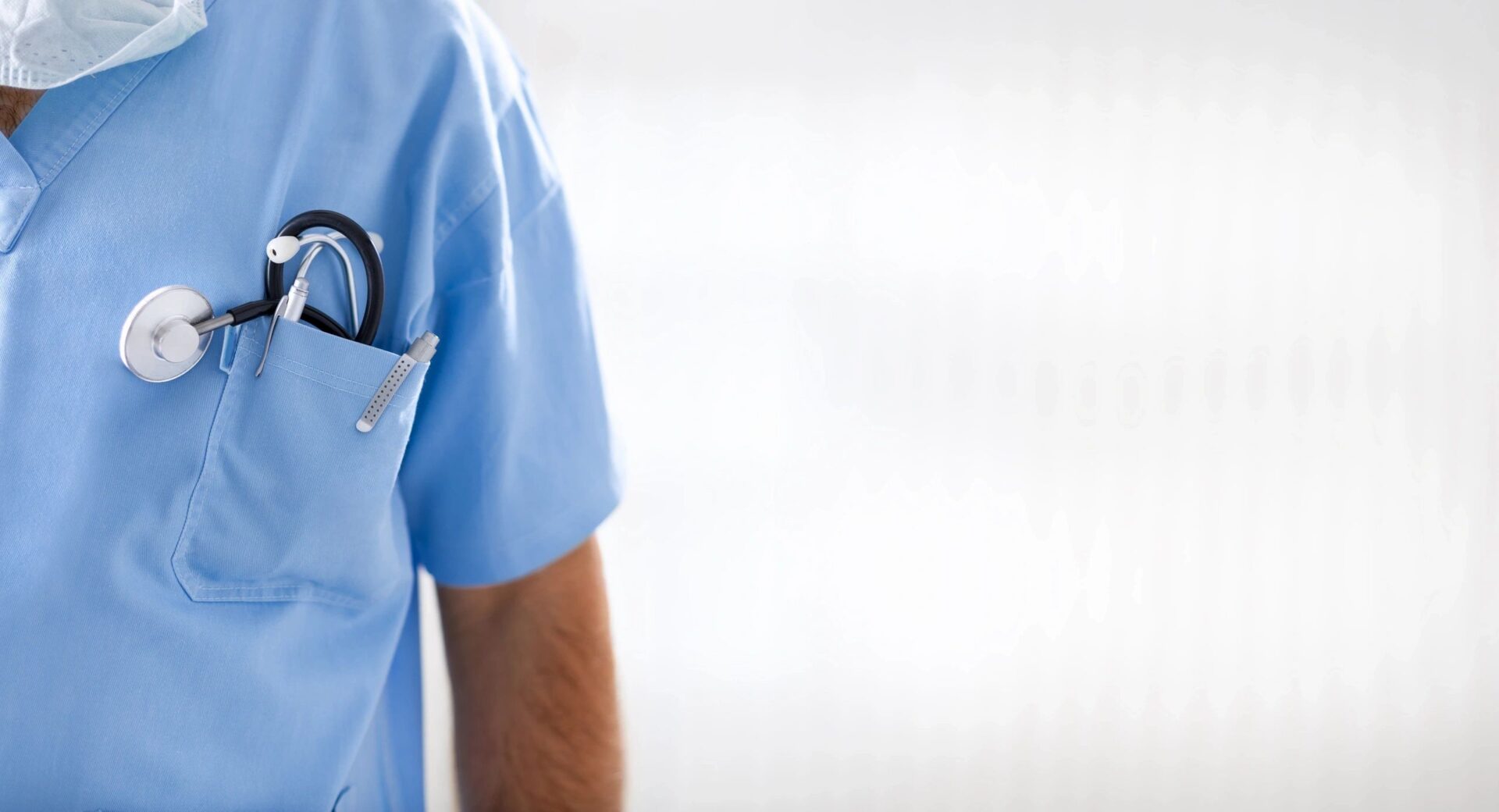A person in blue scrubs holding a stethoscope.