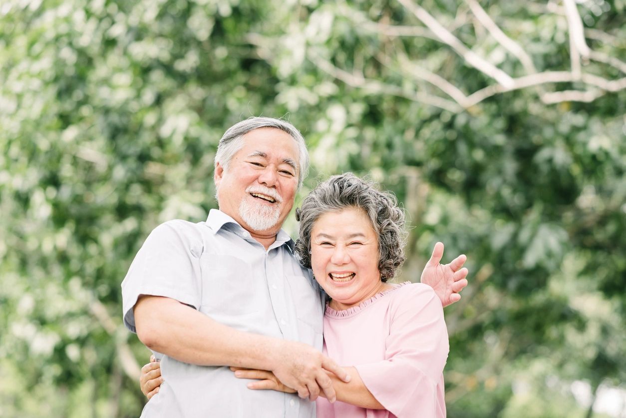 An older couple posing for a picture in front of trees.