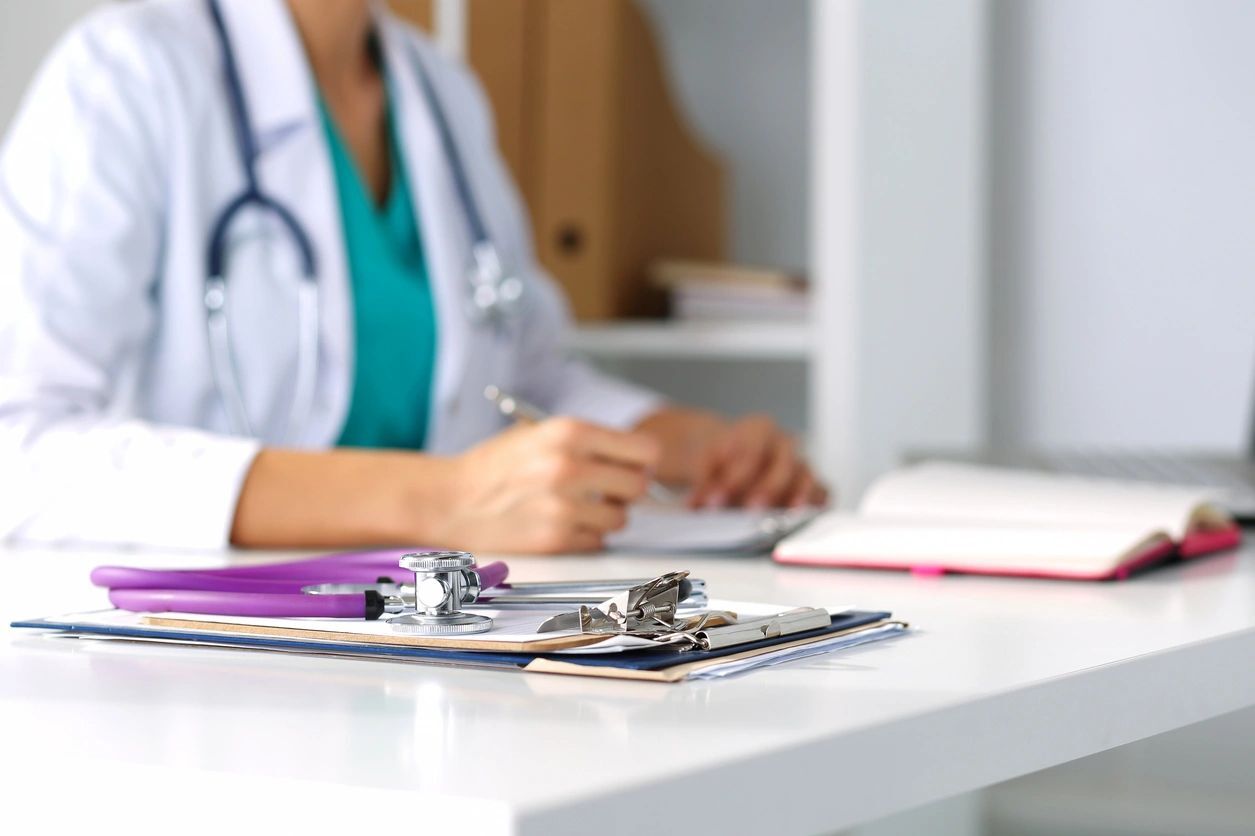 A doctor sitting at the table with papers and a clipboard.