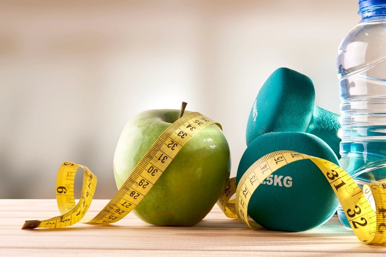 A green apple and measuring tape next to a dumbbell.